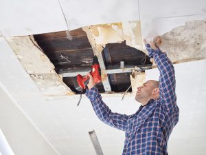 Man with drill fixing ceiling with water damage.